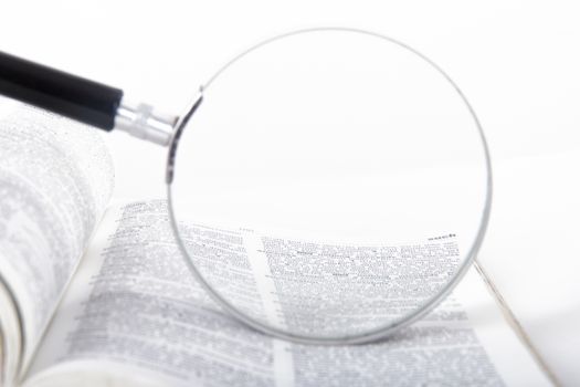 Classic style magnifying glass on open dictionary book, examining the words, isolated on white background.