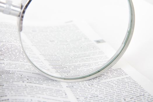 Close up of classic style magnifying glass on open dictionary book, searching words, isolated on white background.