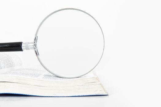 Classic style magnifying glass on open dictionary book, isolated on white background.