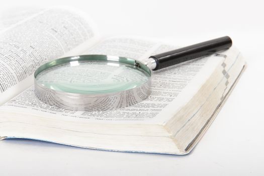 Classic style magnifying glass on open dictionary book, isolated on white background.