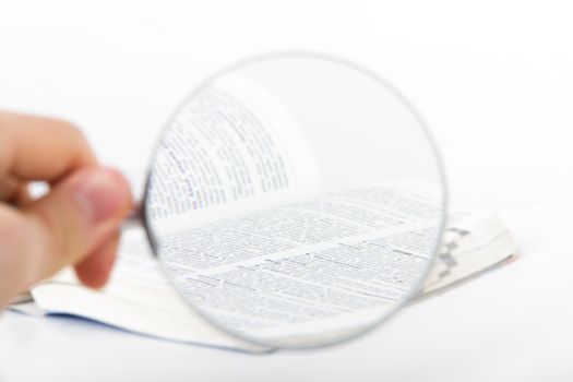 Classic style magnifying glass on open dictionary book, isolated on white background.