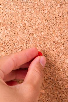 Hand with red push pin on cork bulletin board.