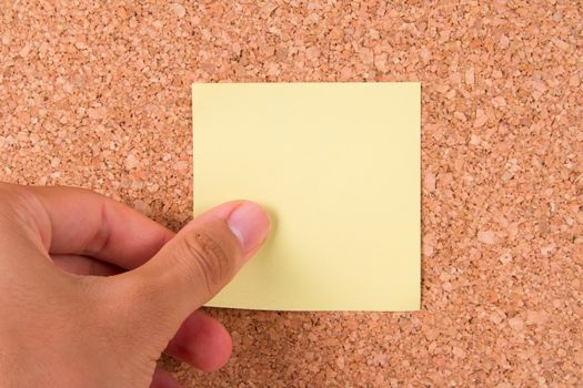 Hand and blank, yellow sticky post it note for your message on cork bulletin board.