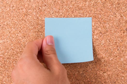 Hand and blank, blue sticky post it note for your message on cork bulletin board.