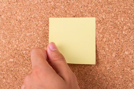 Hand and blank, blue sticky post it note for your message on cork bulletin board.