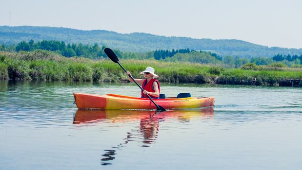 Young Woman Kayaking Alone on a Calm River and Wearing a Safety Vest