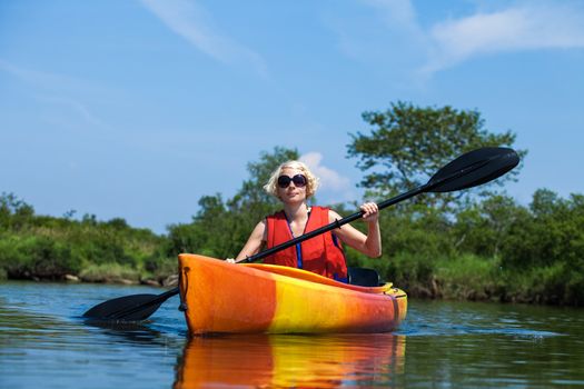 Young Woman Kayaking Alone on a Calm River and Wearing a Safety Vest