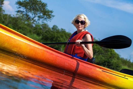 Young Woman Kayaking Alone on a Calm River and Wearing a Safety Vest