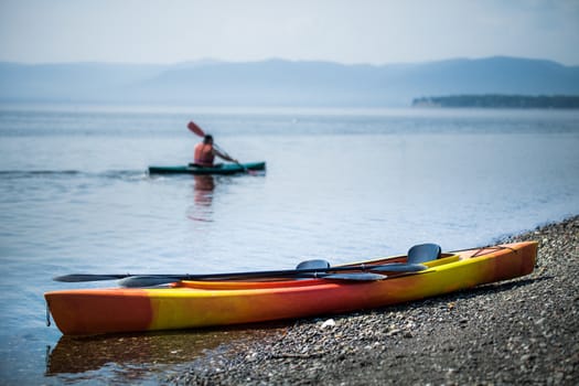 Orange and Yellow Kayak on the Sea Shore During a beautiful Day of Summer with Unrecognizable People Kayaking in the Background