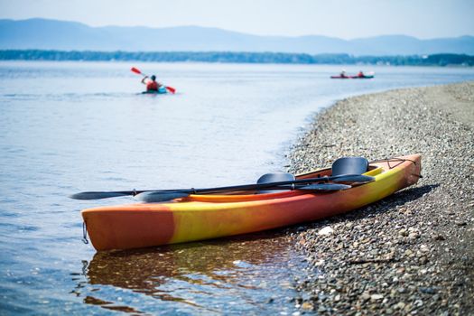 Orange and Yellow Kayak on the Sea Shore During a beautiful Day of Summer with Unrecognizable People Kayaking in the Background