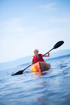 Young Woman Kayaking Alone on a Calm Sea and Wearing a Safety Vest