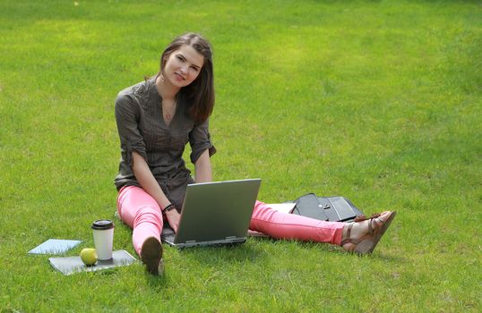 Young woman working on a laptop in a green field of grass.