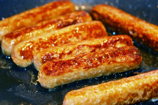 Pork and beef sausages cooked in a frying pan with oil 