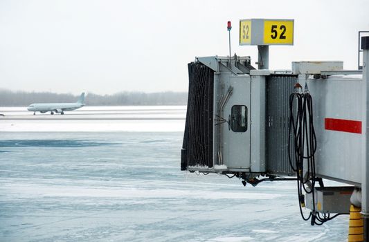 Cold snowing winter day, ice on the frozen tarmac, airplane in the back and docking station in the front.