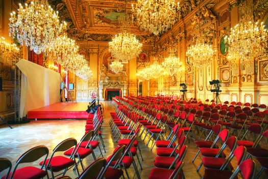 Preparing a press conference in an antique castle ballroom with crystal chandelier, gold paintings and red velvet chairs. hdr
