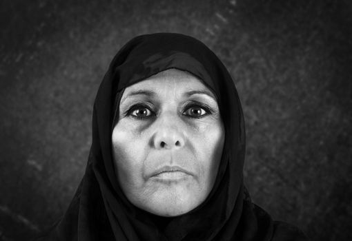 Dramatic blackand white portrait of serious middle aged muslim woman with black scarf or hijab