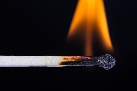 Close up of burning, flaming match on fire against black background.