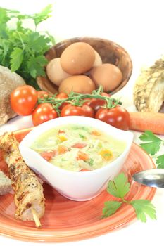 Chicken soup with eggs, noodles, greens and tomatoes on bright background