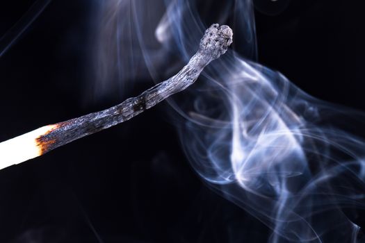 Burnt match with smoke on dark background.