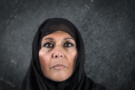 Dramatic portrait of serious middle aged muslim woman with black scarf or hijab