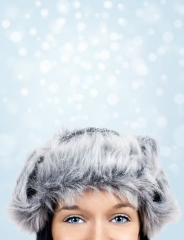 Beautiful young woman with stunning eyes and fur hat over winter snow background