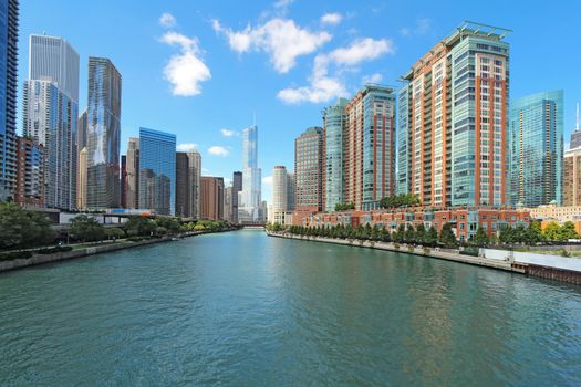 The city skyline along the Chicago River in Chicago, Illinois against a bright blue sky with white clouds