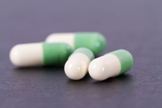 Green and white medical capsules on black wooden table.