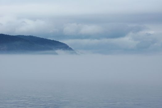Thick fog over water with mountains and clouds, great landscape.