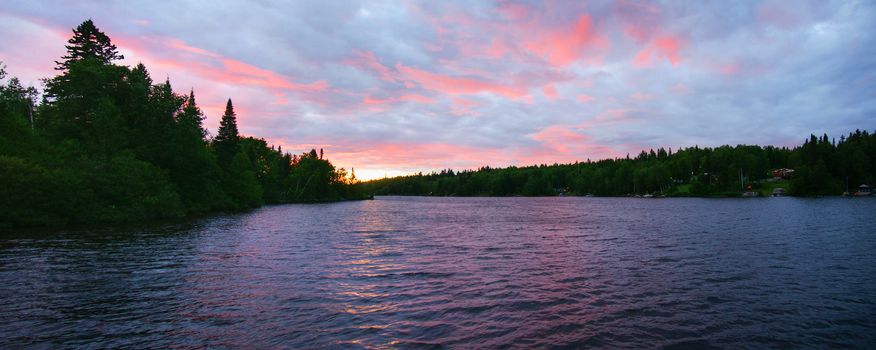 Panorama of pink sunset on a northern lake with cottages on shore