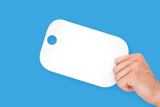 Hand holding white, empty, blank shopping label cardboard, isolated on blue background.