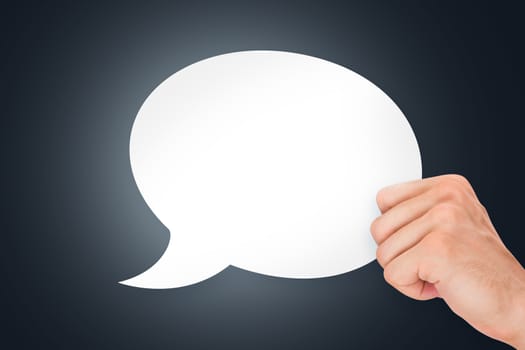 Human hand holding white, empty, blank speech bubble on dark background.