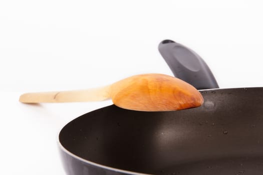 Close up of frying pan and wooden spoon, isolated on white background.