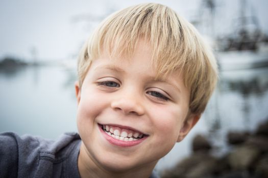 A happy little 5 year old smiling for the camera on the rocks at the harbor on an overcast day.