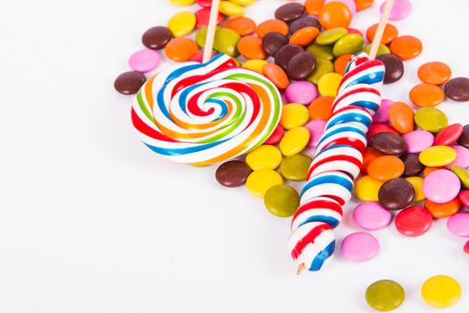 Colorful spiral lollipop candy on stick and little sugars with copy space, isolated on white background.