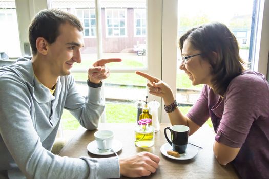 Young man and woman pointing each other while sitting at cafe