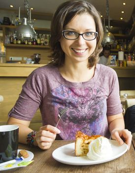 Smiling woman at cafe eating apple cake dessert with cream