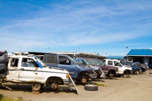 The scene shows many cars and other automobiles in a salvage junk yard where customers can pick and choose part for their vehicle repairs.