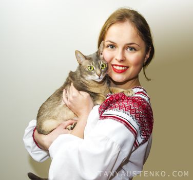 Portrait of beautiful young woman in the Ukrainian national clothes with cat against gray backgraund