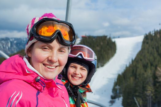 Portrait of happy woman in ski goggles and a helmet with daughter on the ski lift