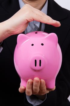 Business woman holding and covering pink piggy bank.