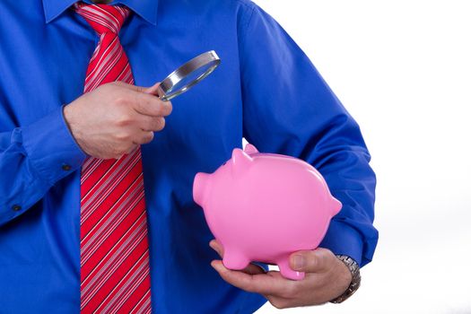 Businessman with red tie examining pink piggy bank with magnifying glass, isolated on white background.