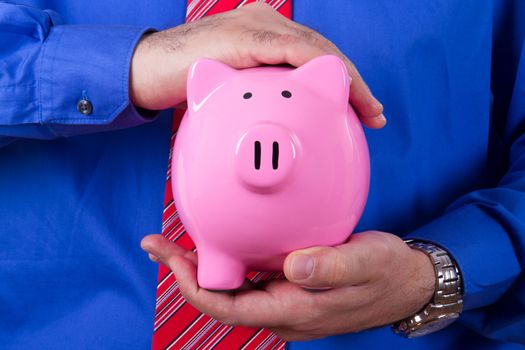 Businessman with blue shirt covering and protecting pink piggy bank with his hands.