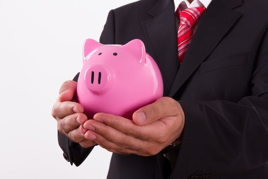 Businessman in a suit holding pink piggy bank with both hands, isolated on white background.
