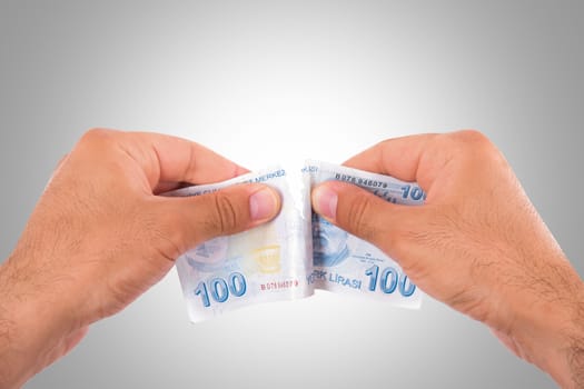 Hands tear one hundred Turkish lira banknote, isolated on white background.