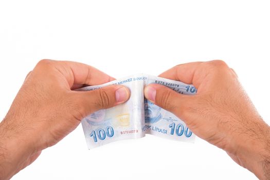 Hands tear one hundred Turkish lira banknote, isolated on white background.
