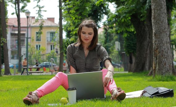 Young woman working on a laptop outside in an urban park.