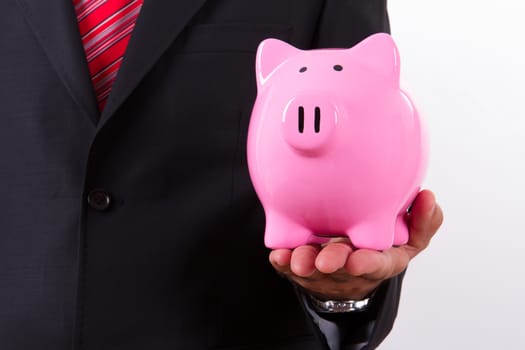 Businessman in suit holding pink piggy bank with left hand, isolated on white background.