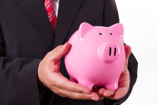 Businessman in suit holding pink piggy bank with both hands, isolated on white background.