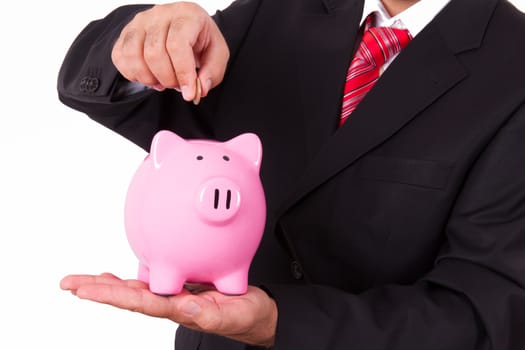 Businessman putting coin into pink piggy bank, isolated on white background.