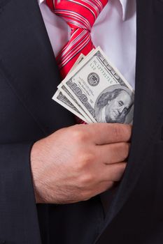 Businessman in a black suit putting money in his pocket.